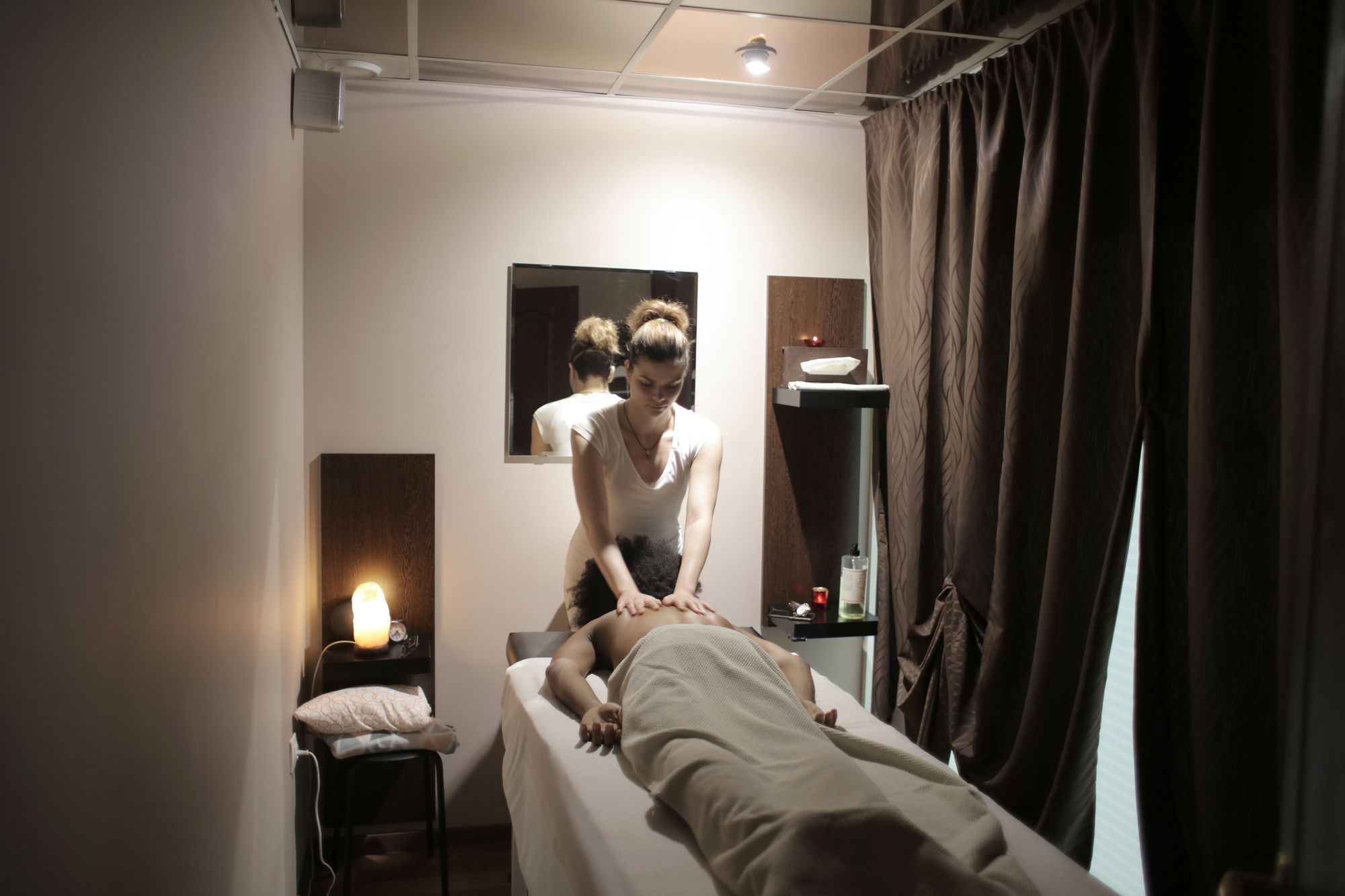 A therapist giving a back massage to a guest in a warmly lit spa treatment room