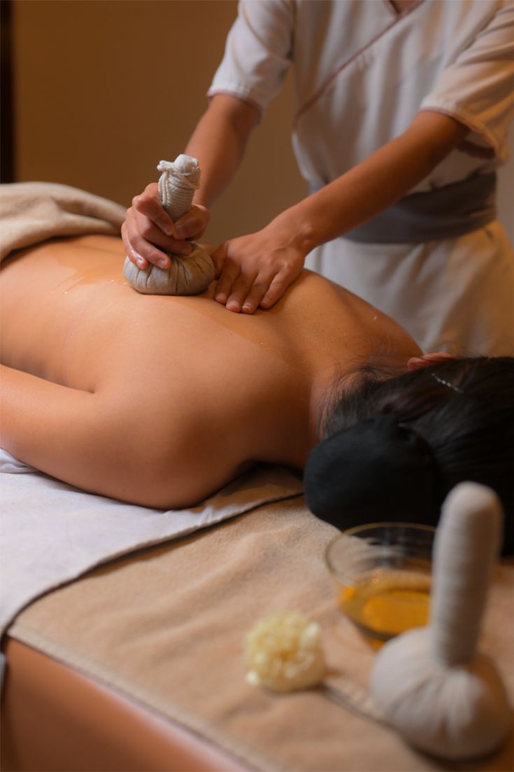 Therapist pressing a warm herbal poultice along a guest’s back during Podi Kizhi