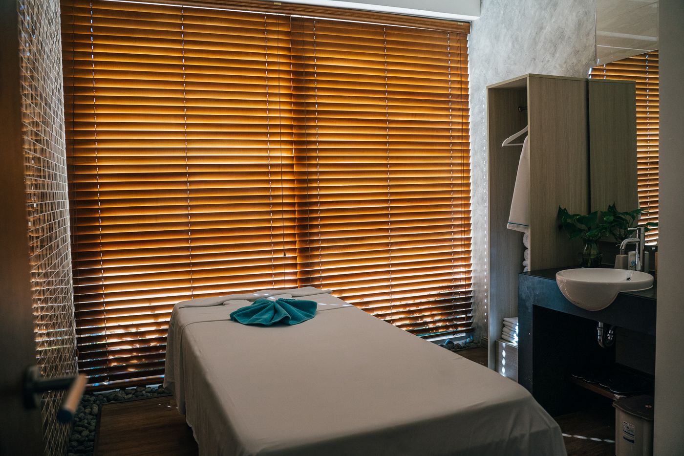 A treatment room with a dressed massage table lit by warm wooden blinds